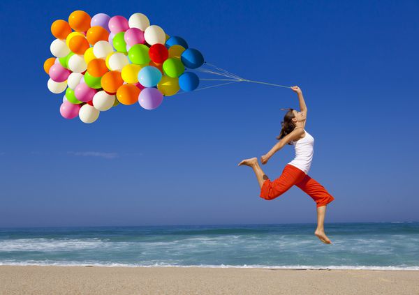 دختر زیبا و ورزشی با بالن های رنگارنگ که در ساحل می پرند