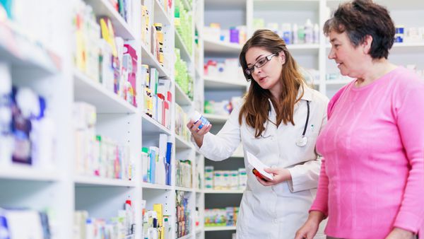 داروساز زن در مورد داروهای تجویز شده با مشتری ارشد داروخانه بحث می کند