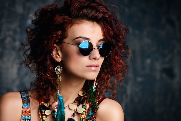 پرتره نزدیک از یک زن زیبا و روشن با موهای روباه فرفری در عینک آفتابی گوشواره و مهره سبک قومی در لوازم جانبی