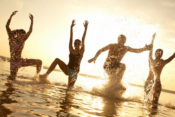 گروهی از جوانان که در غروب آفتاب زیبا تابستان در حال و سمپاشی در ساحل هستند