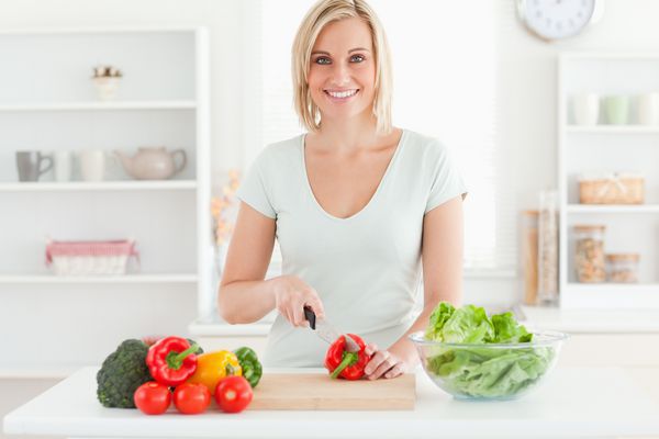 زن جوان سبزیجات برش لبخند در آشپزخانه به دوربین
