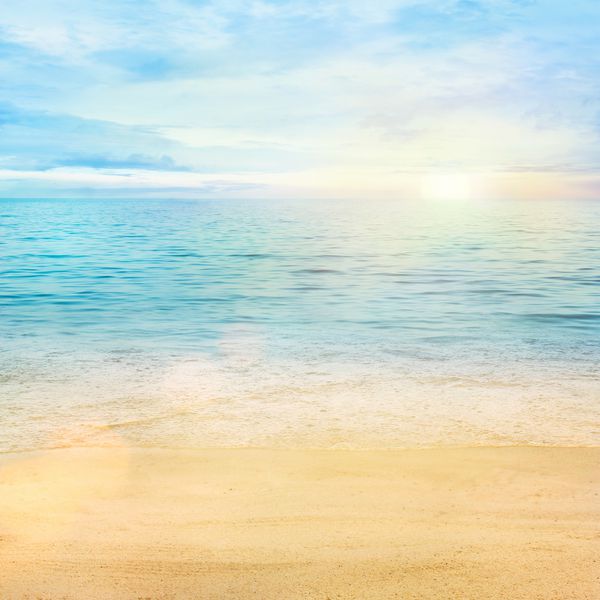پس زمینه انتزاعی تابستان یا بهار زیبا دریا ساحل ماسه ای طلایی با اقیانوس آبی و فضای ابری و غروب خورشید در پشت