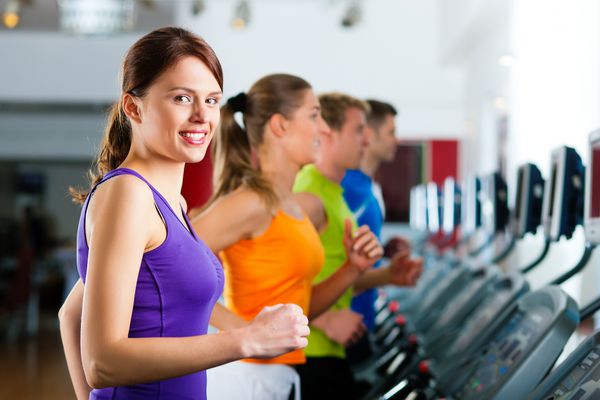 دویدن بر روی تردمیل در سالن بدنسازی یا باشگاه بدنسازی گروهی از زنان و مردانی که برای کسب آمادگی بیشتر ورزش می کنند