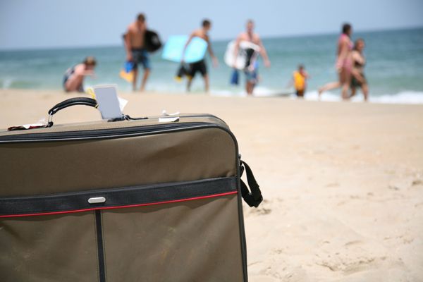 عکس مفهومی سفر تعطیلات با یک چمدان در ساحل