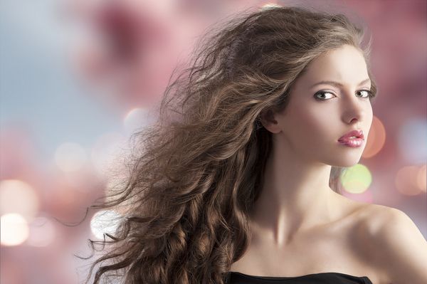 پرتره مد زیبایی از ناز بسیار جوان با موهای مجعد بلند با مدل موهای پرواز در باد در پس زمینه شکوفه گیلاس بوکه