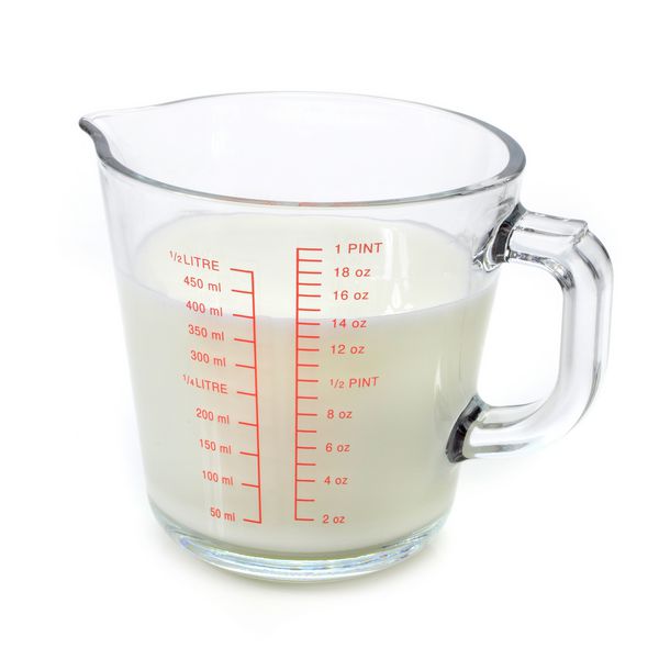 شیر در اندازه گیری فنجان بر روی زمینه سفید