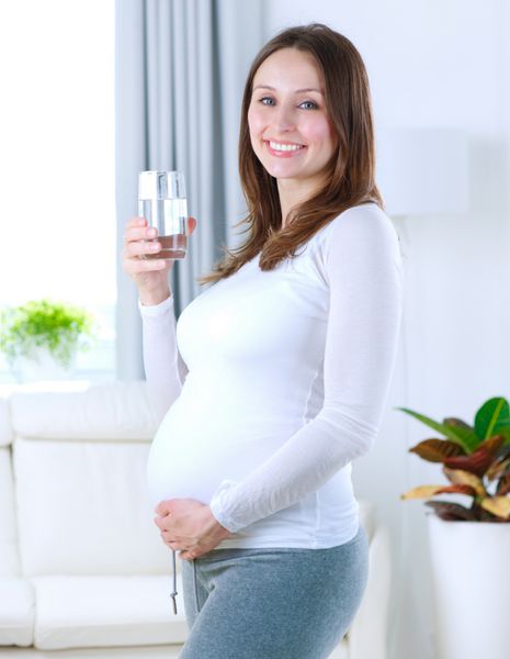 زن جوان باردار که در حال نوشیدن آب شیرین در خانه است بارداری سالم
