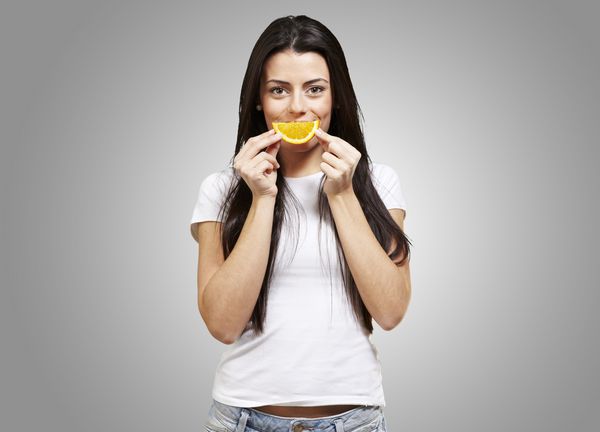 زن با یک برش نارنجی به عنوان یک لبخند در برابر پس زمینه خاکستری