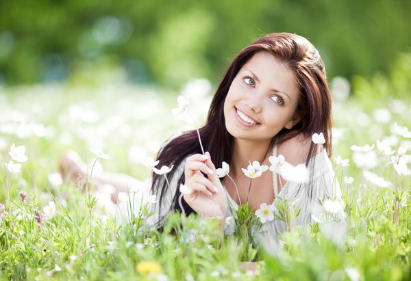 یک زن جوان زیبا که در یک روز گرم تابستان روی گلزار با گلهای سفید آرامش می یابد