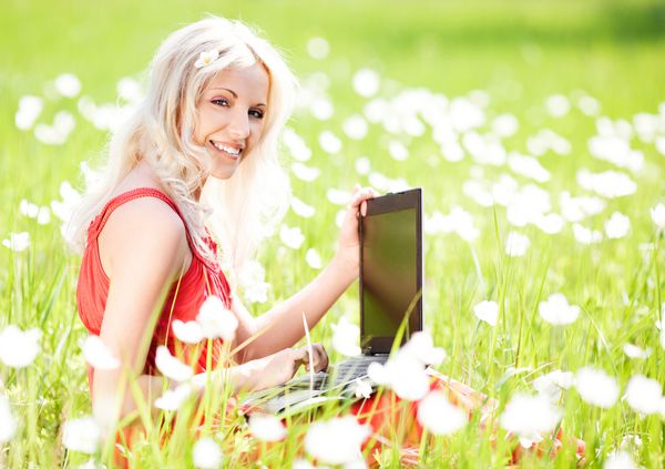 یک زن جوان زیبا با یک لپ تاپ در پارک در یک روز گرم تابستان