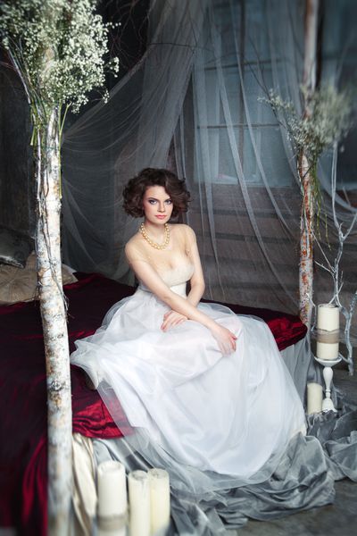 عروس افسونگر در لباس بلند و روان که روی یک تخت در یک فضای مرموز با شمع ها نشسته است