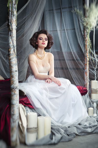 عروس افسونگر در لباس بلند و روان که روی یک تخت در یک فضای مرموز با شمع ها نشسته است