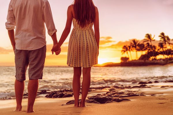 زوج ساحلی که دستان غروب آفتاب را تماشا می کنند افرادی که از پشت سر می گذرانند از تعطیلات سفر تابستانی در مقصد گرمسیری لذت می برند