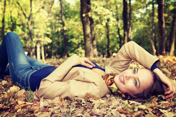 دختر جوانی که در پاییز با برگ ها لبخند می زند