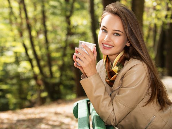 دختر جوان زیبا پارک پاییزی قهوه می نوشد
