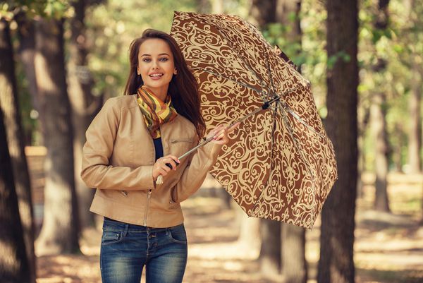 دختر جوان در پاییز با چتر لبخند می زند