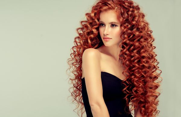 دختر مدل زیبا با موهای فرفری قرمز قرمز بلند دست سر محصولات مراقبت از مو و زیبایی