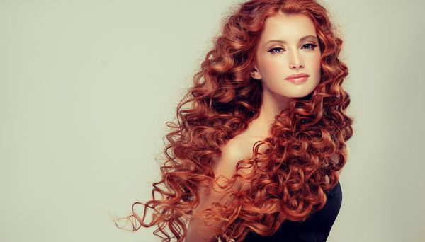 دختر مدل زیبا با موهای فرفری قرمز قرمز بلند دست سر محصولات مراقبت از مو و زیبایی
