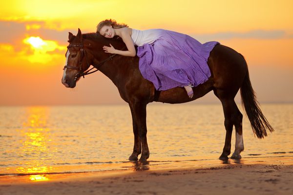 زن زیبا سوار بر اسب در غروب آفتاب در ساحل زن جوان