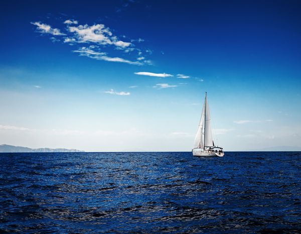 بادبان های سفید قایق بادبانی بر روی زمینه دریا و آسمان در ابرها