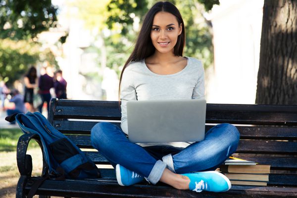 دانش آموز زن که با لپ تاپ روی نیمکت نشسته است