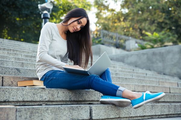 دختری که با لپ تاپ در فضای باز در پله های شهر نشسته است