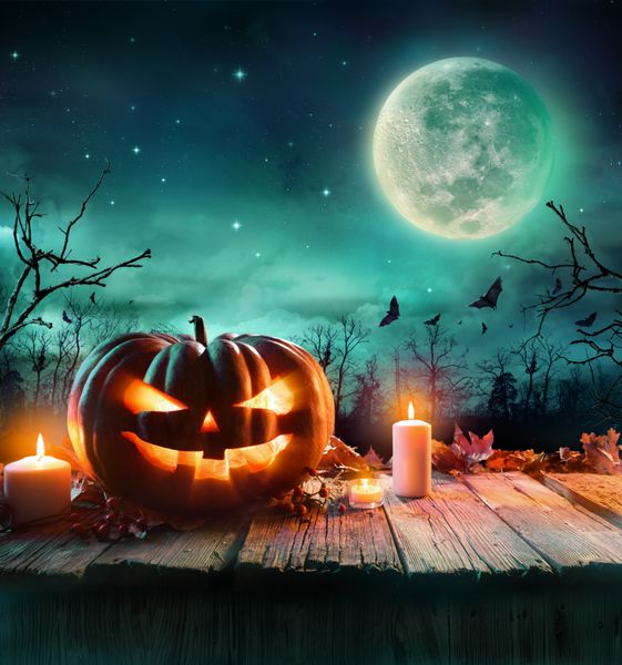 کدو تنبل هالووین در تخته چوبی با شمع ها در یک شب شبح وار