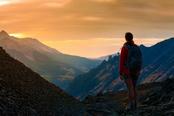 دختر کوله پشتی که به کوههای غروب آفتاب کلرادو می رود