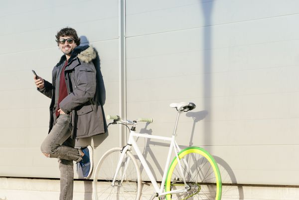 مرد جوان خوش تیپ با تلفن همراه و دوچرخه دنده ثابت