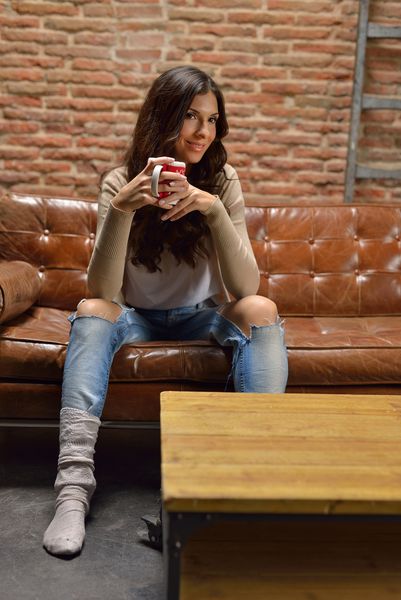 Mujer joven con taza de caf amp eacute؛ sentada en el sof amp aacute؛