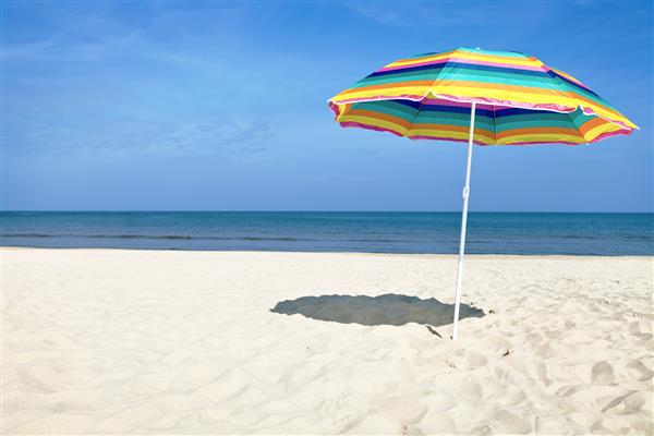 چتر ساحلی رنگارنگ در روز تابستان در ساحل شنی آسمان آبی و دریا در پس زمینه