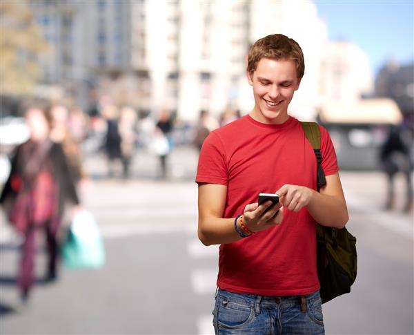 پرتره مرد جوان در حال لمس صفحه تلفن همراه در خیابان شلوغ