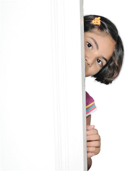دختر بچه هندی آسیایی خجالتی که پشت در مخفی شده است