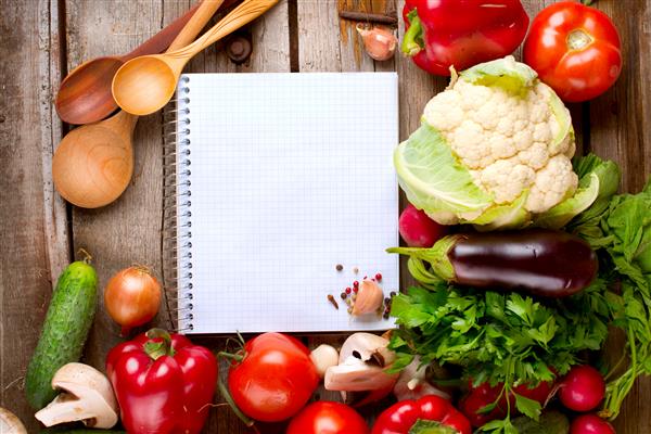 سبزیجات و ادویه جات در یک زمینه چوبی و کاغذ برای یادداشت ها دفترچه یادداشت باز و سبزیجات تازه رژیم غذایی رژیم غذایی فضای متن شما