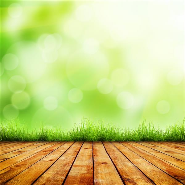 چمن سبز بهاری تازه با بوکه سبز و نور خورشید و کف چوب زمینه طبیعی زیبایی