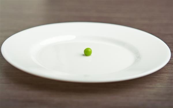 مفهوم رژیم غذایی یک نخود سبز روی یک صفحه سفید خالی