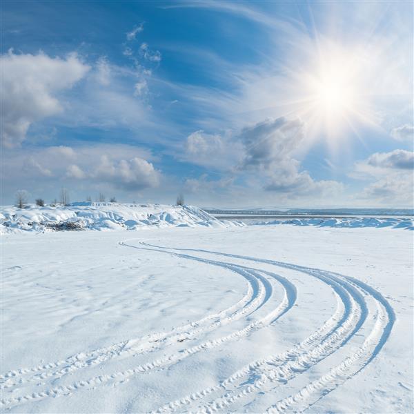 چشم انداز زمستانی با رد پای لاستیک در برف که به آسمان خورشید و ابرها می رود