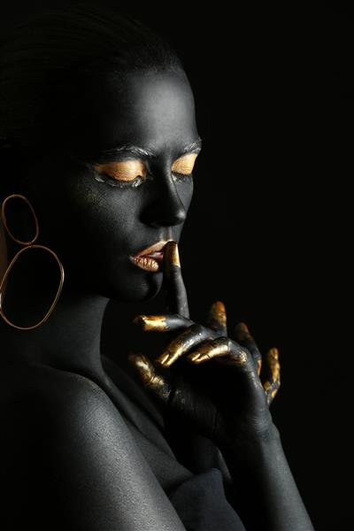 زن زیبا با رنگ سیاه و طلایی روی بدن در برابر پس زمینه تیره