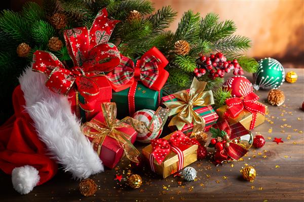 ترکیب تعطیلات کریسمس با کلاه قرمز بابانوئل توپهای کریسمس و جعبه های کادو در زمینه چوبی