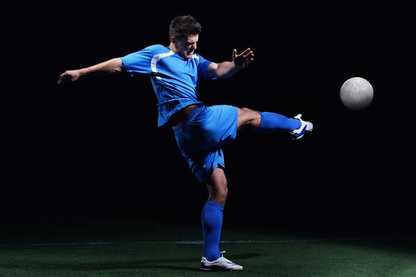 بازیکن فوتبال در زمین ورزشگاه فوتبال که روی پس زمینه سیاه قرار دارد با پا زدن می کند