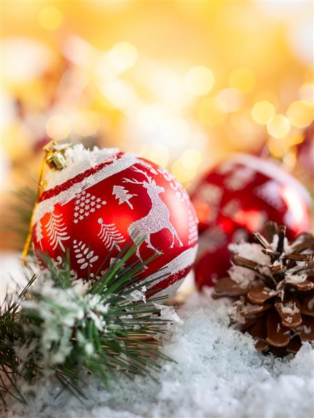 توپهای کریسمس قرمز با تزئینات و شاخه های صنوبر با مخروط کاج در زمینه براق طلایی