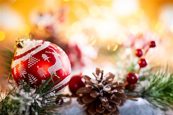 توپهای کریسمس قرمز با تزئینات و شاخه های صنوبر با مخروط کاج در زمینه براق طلایی