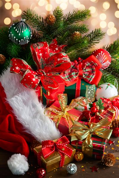 ترکیب تعطیلات کریسمس با کلاه قرمز بابانوئل توپهای کریسمس و جعبه های کادو در زمینه چوبی