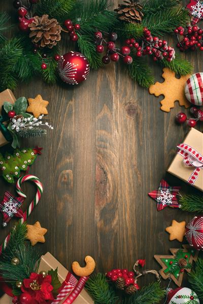 قاب با شاخه های صنوبر کلوچه ها و تزئینات کریسمس در زمینه چوبی تیره نمای بالا