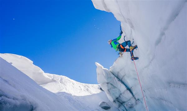 عکس حماسی از کوهنورد یخی در حال بالا رفتن روی دیواره یخ کوهنورد کوهنورد یا کوهنورد در یک صعود شدید ماجراجویی با تبر یخ و کرامپون کوهنوردی شدید آلپ بر روی سرا یا شکاف