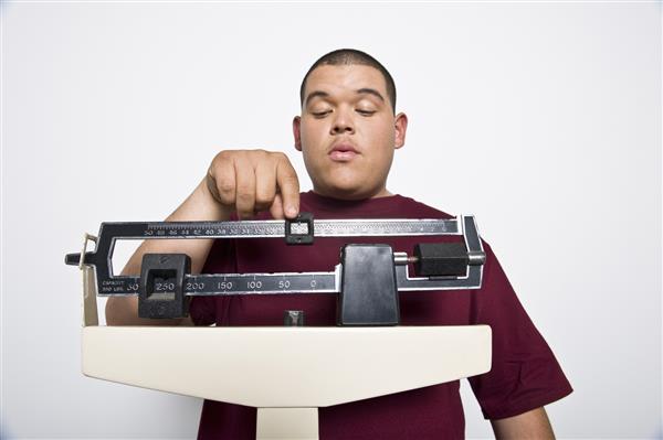 مرد جوانی که وزن خود را در مقیاس توزین در کلینیک اندازه گیری می کند