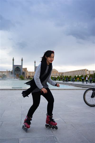اصفهان ایران یک زن جوان مسلمان زیبا و شیک پوش ایرانی در حال اسکیت غلتکی در میدان نقش جهان در مرکز شهر اصفهان است