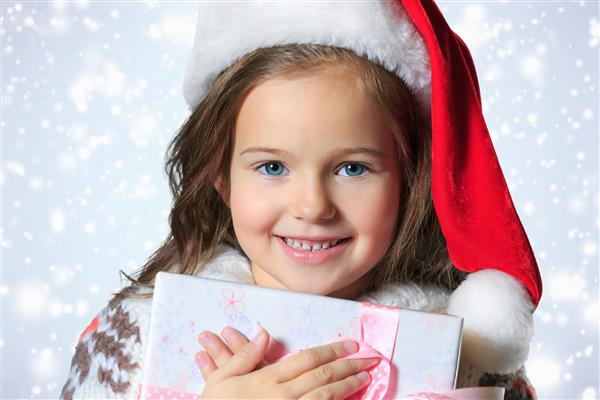دختر کوچک زیبا با کلاه بابانوئل نزدیک درخت کریسمس