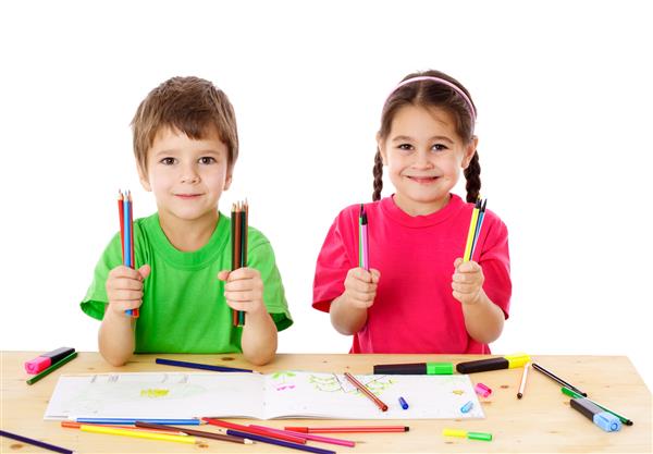 دو کودک کوچک خندان روی میز با مداد رنگی جدا شده روی سفید