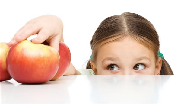 دختر کوچک ناز روی میز سیب منزوی شده روی سفید است